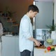 Young Man Cooking Food While Woman Speaking on Mobile Phone in Kitchen in Apartment - VideoHive Item for Sale