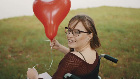 Disabled Caucasian Young Woman with Red Balloon Looking Over the Shoulder and Smiling 