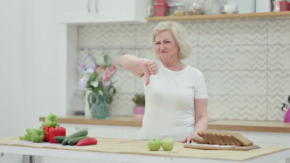 Old Woman Showing Thumbs Down While Standing in Kitchen