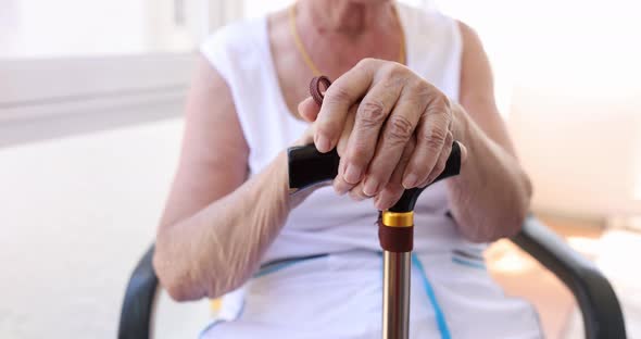 Elderly Woman in Sitting in a Chair Leans on a Cane