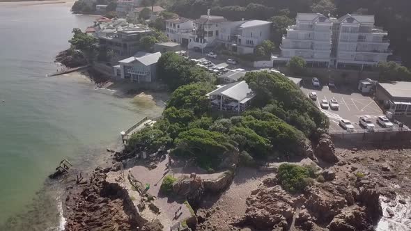 Lighthouse and restaurant at rugged rocky headland, rotating aerial