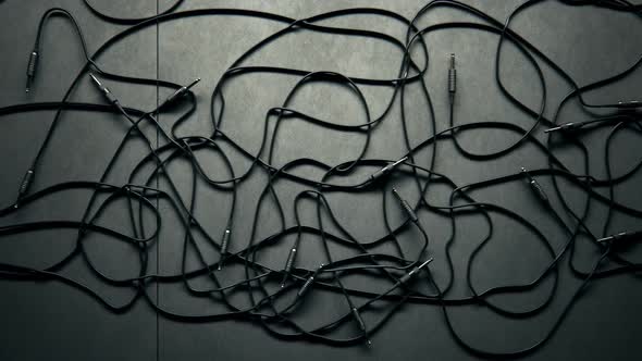 Bunch of tangled black audio cables with jack plugs lying on grey studio floor.
