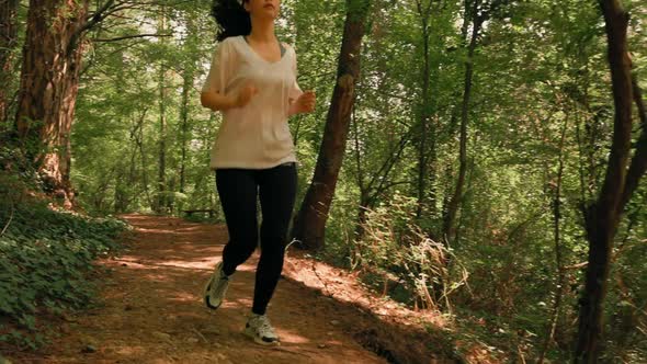 Sporty woman in sports clothes is jogging at forest path.Slow motion. Low angle. Pan shot