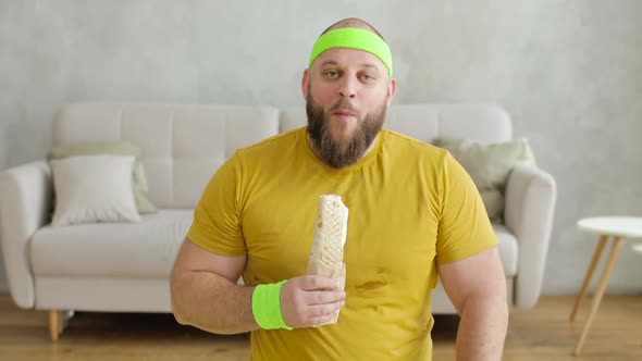 Fat Man Is Eating Danar Sitting on Fitness Mat at Home After Sport Exercises