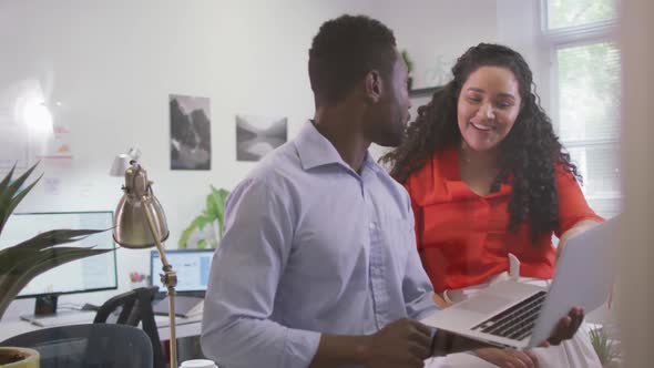 Two happy diverse business people working together, using laptop in modern office