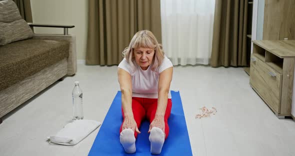 Elderly Woman Doing Stretching Exercises at Home Seated on a Mat in the Living Room Reaching