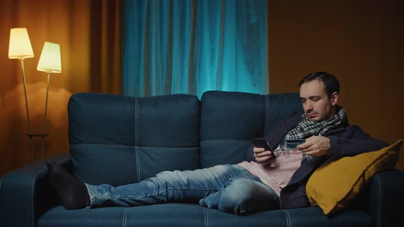 Man Lies on a Cozy Sofa and Makes Payment Online By Credit Card