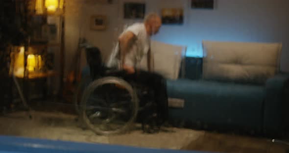 Disabled Man Transferring From Wheelchair To Sofa