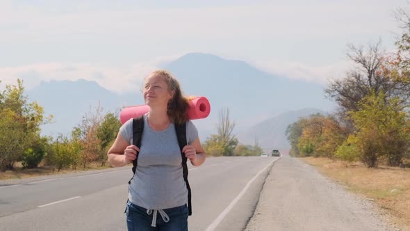 Happy Tourist Goes on Road on Background of Mountains.