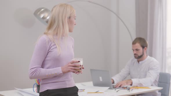 Beautiful Young Caucasian Woman Drinking Cappuccino or Latte, Turning Back and Talking To Her Male