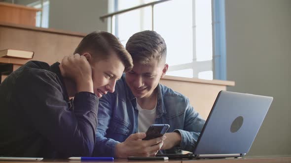 Pretty Girls Students are Using Smartphone Watching Screen Talking and Laughing Sitting at Desks at