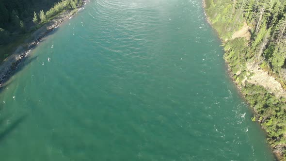 Aerial Shoot tilitng up of Revelstoke Dam at noon, Surrounded by Mountrains and Pine Trees