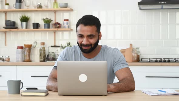 Happy Excited Lucky Indian Man in Casual Wear Freelancer Sits at a Desk in Kitchen Work From Home