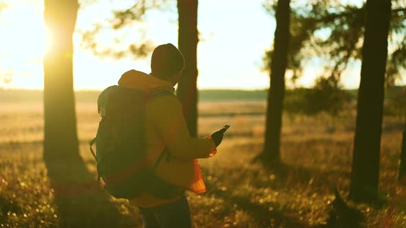 Man Hiker Backpacker Traveler Camper with Her Phone Looks at a Map or Route Under Sun Light