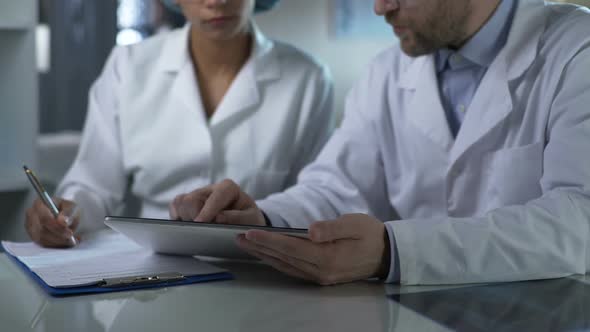 Physician Giving Instructions to Assistant, Checking Test Results on Tablet