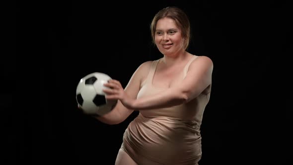 Portrait of Joyful Caucasian Plus Size Woman Smiling Dancing with Soccer Ball at Black Background