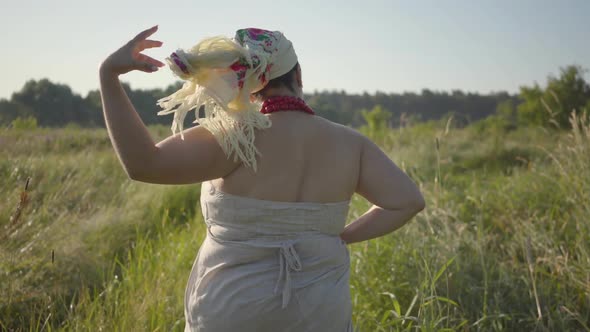 Back View of Overweight Woman Taking Off Shawl, Unbinding Hair and Running on Summer Field. Woman