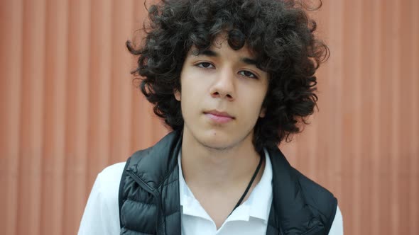 Portrait of Curlyhaired Teenager Looking at Camera with Serious Face Standing Outdoors Alone