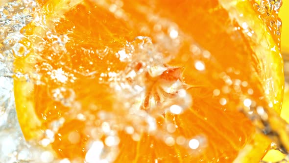 Super Slow Motion Detail Shot of Rotating Fresh Orange Slice and Splashing Water at 1000Fps