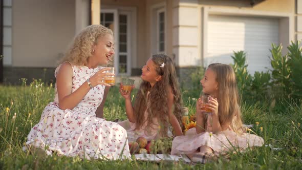 Wide Shot Happy Family Toasting Juice Sitting on Picnic on Backyard at Sunset