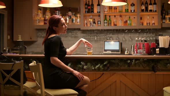 Lonely young woman sits in an empty bar in the evening and drinks