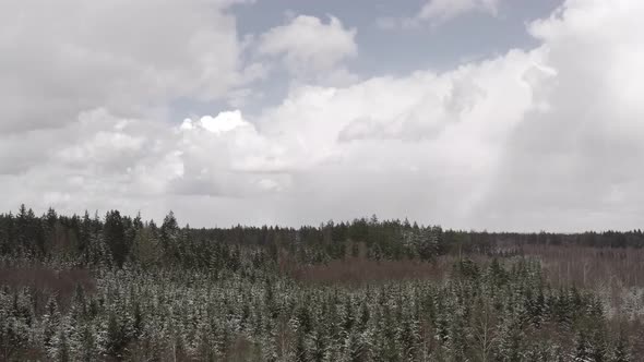 Flying forward in a light snowfall over a rural forest landscape by my drone under a cloudy blue sky