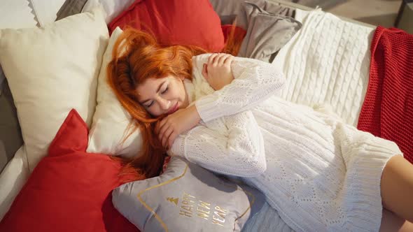 Cozy Sexy Red-haired Woman in White Knitted Sweater Lies on Sofa. Happy New Year