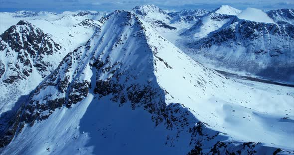 Ascending aerial panorama shot over snowy mountain landscape during sunshine and blue sky in Winter