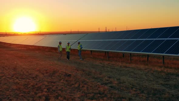 Three Solar Energy Specialists Walking Through a Solar Park at Bright Sunset