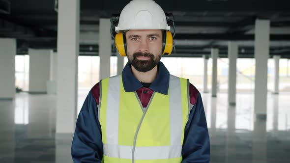 Slow Motion Portrait of Builder Wearing Safety Clothing and Headphones Standing in Commercial