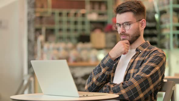 Pensive Young Man Using Laptop in Cafe