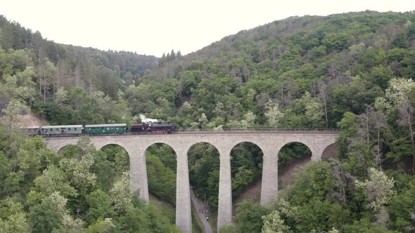 Steam train passing over a stone viaduct in a mountain valley,zooming.