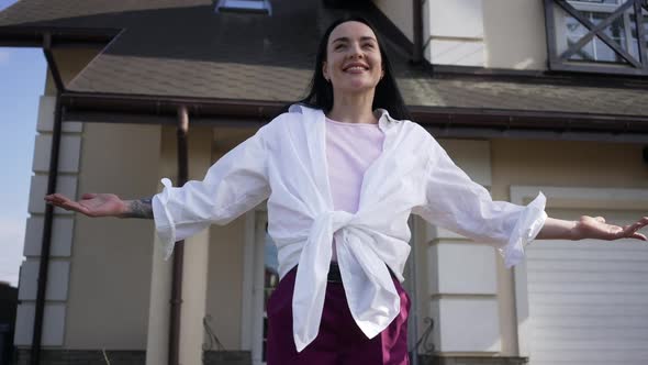 Tattooed Happy Caucasian Woman Stretching Hands Standing on Front Yard at New House