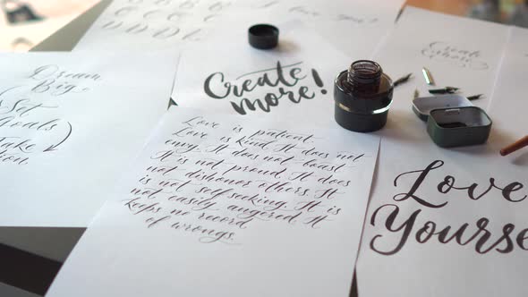 Closeup Shot of a Calligraphy Tools and a Bottle of Ink and Sheets of Paper with Different Writings