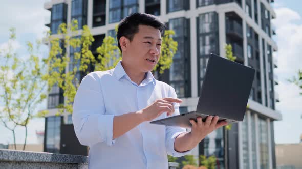 Male Asian Makes Conference Chat Interview Using New Technology in City Park