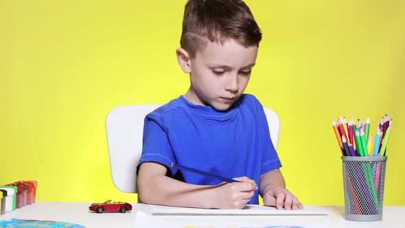 The boy sits at the table and draws with colored pencils. Creative child. The preschooler draws