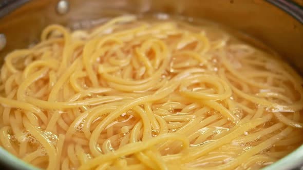 Raw spaghetti is being cooked in boiling water in a kitchen pot.