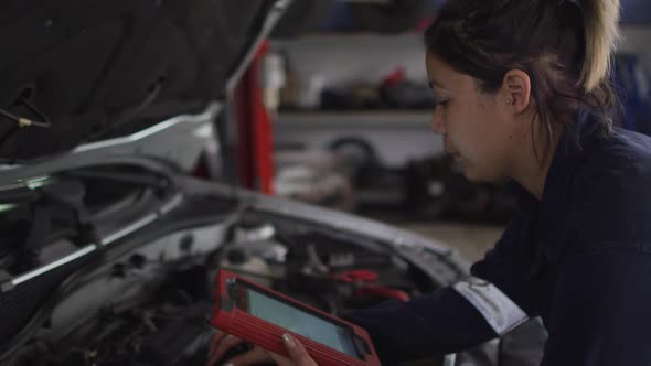 Female mechanic using digital tablet and inspecting the car at a car service station