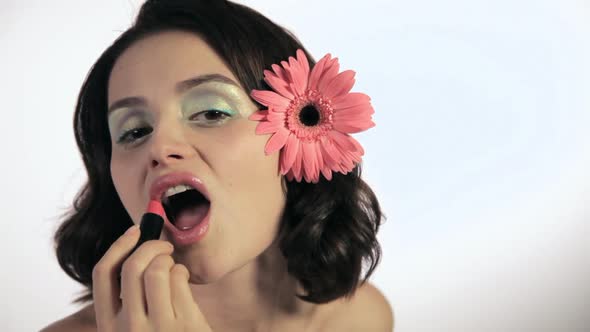 Young woman with flower in hair applying lipstick