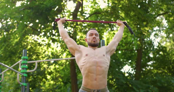 Handsome Muscular Man Training with Elastic Bands at Sports Ground in Park