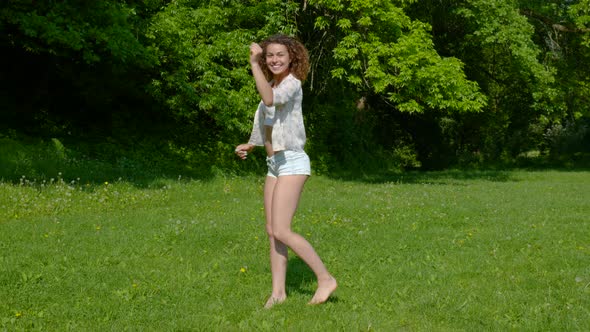 A Young Beautiful Woman Dancing on the Grass in the Park