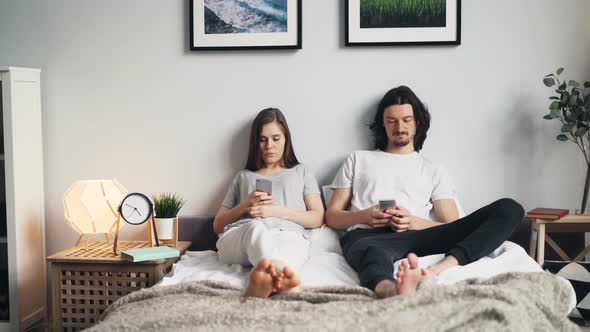 Beautiful Couple Using Smartphones in Bed at Home Touching Screens