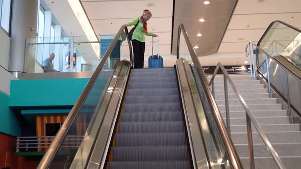 Woman pulling luggage gets on an escalator at an airport.