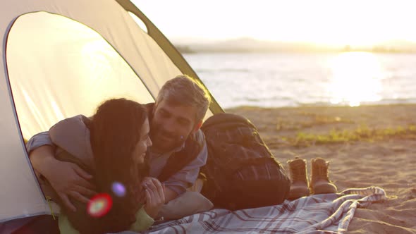 Romantic Couple Embracing and Talking in Tent on Beach at Sunset
