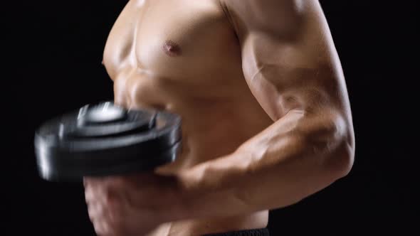 Man Flexes His Hands with Dumbbells Training His Biceps on a Black Background in the Studio