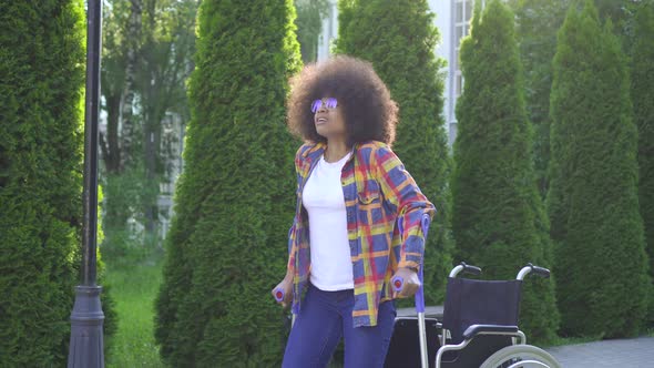 African Woman with an Afro Hairstyle Gets Up From a Wheelchair After an Injury