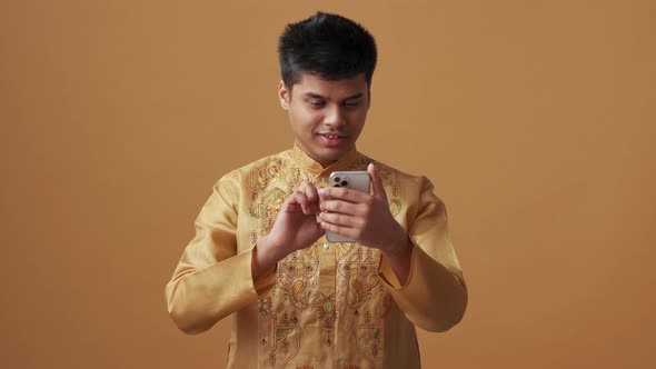 Happy Indian man in national cloth looking at phone