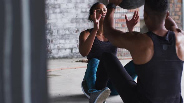 African american man and woman exercising with medicine ball in an empty urban building