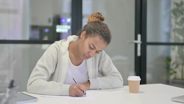 African Woman Writing on Paper in Office