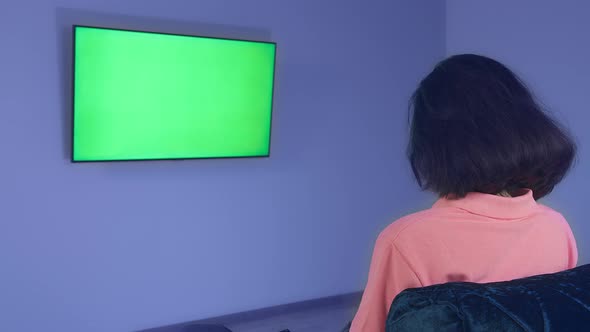 Girl Sitting in Front of a TV Hanging on the Wall Watching News Chromakey Rear View